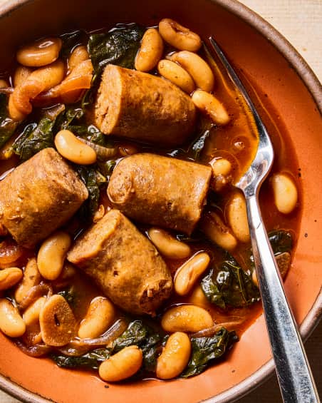 A bowl with spicy sausage, kale, and beans.